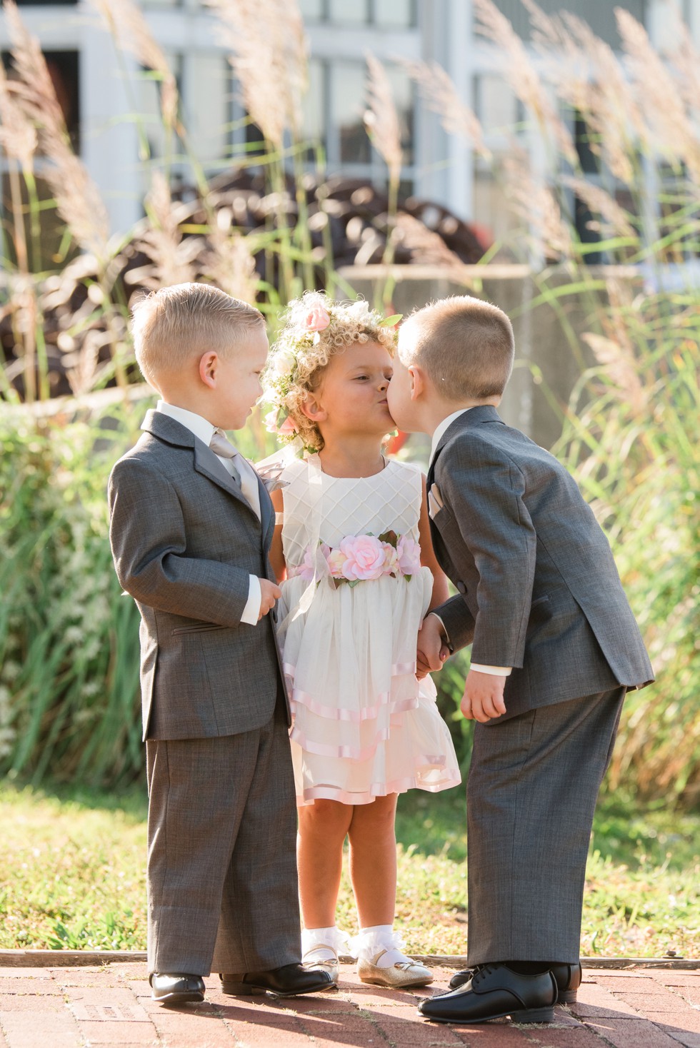 Ring bearer kissing flower girl in the sunshine and grey suits