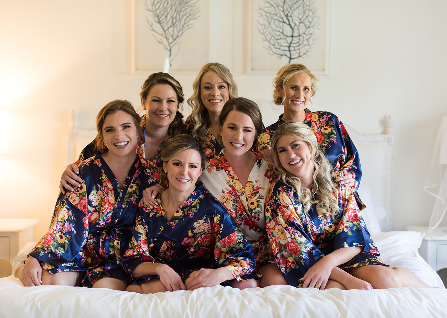 bridesmaids smiling as they all huddle up around the bride as they sit on the bed