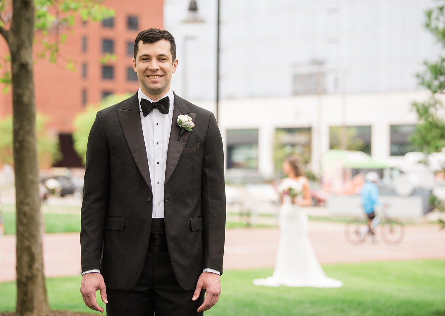 groom facing the camera as his bride stands behind him getting ready to surprise him for their first look