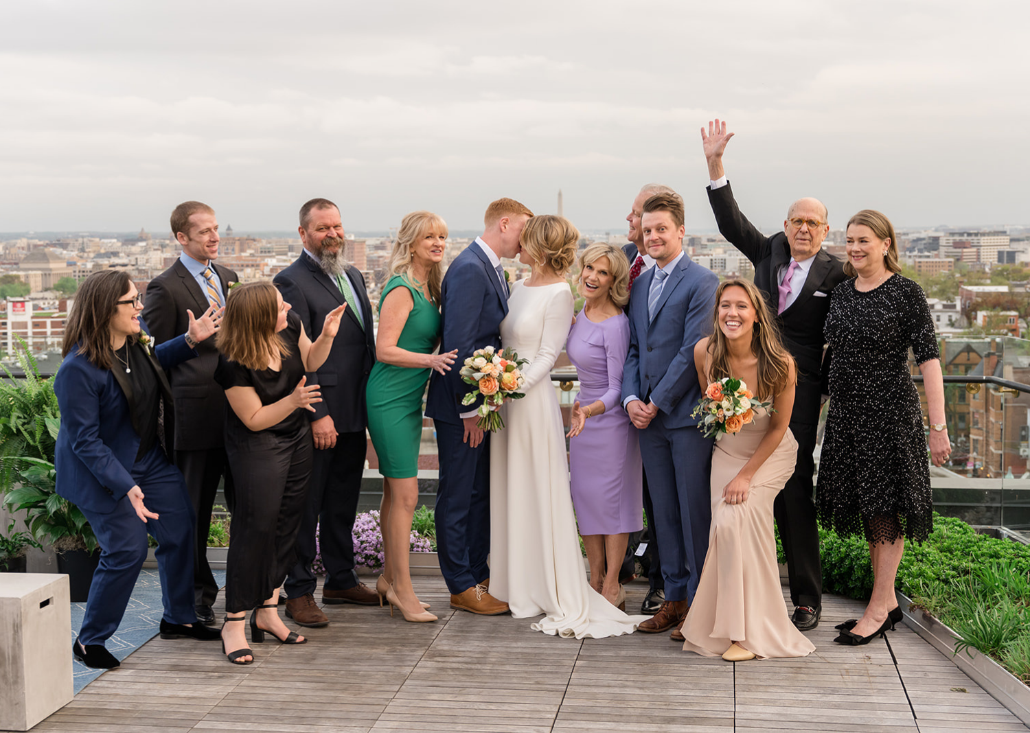 bride and groom share a kiss on the rooftop of the Line Hotel as their family gathers around them celebrating