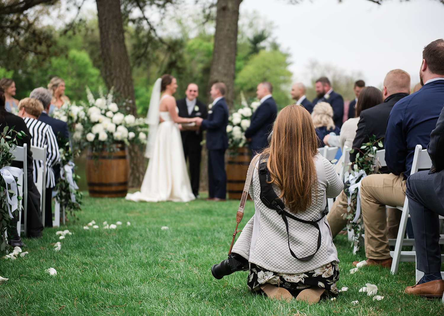 bride and groom during their wedding ceremony as their wedding photographer kneels down to grab the perfect angle