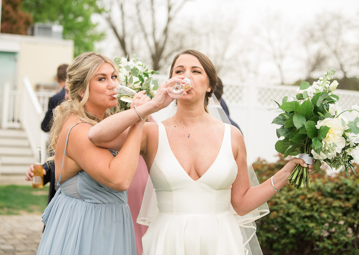 bride takes a drink along with her bridesmaid