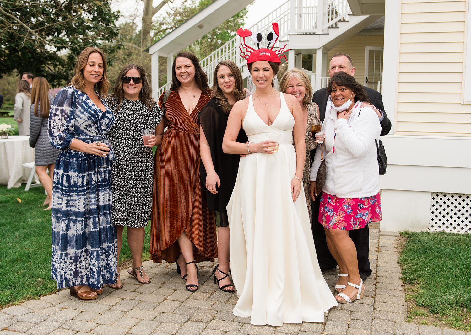 bride is wearing a funny crab hat as she is surrounded by her friends and family