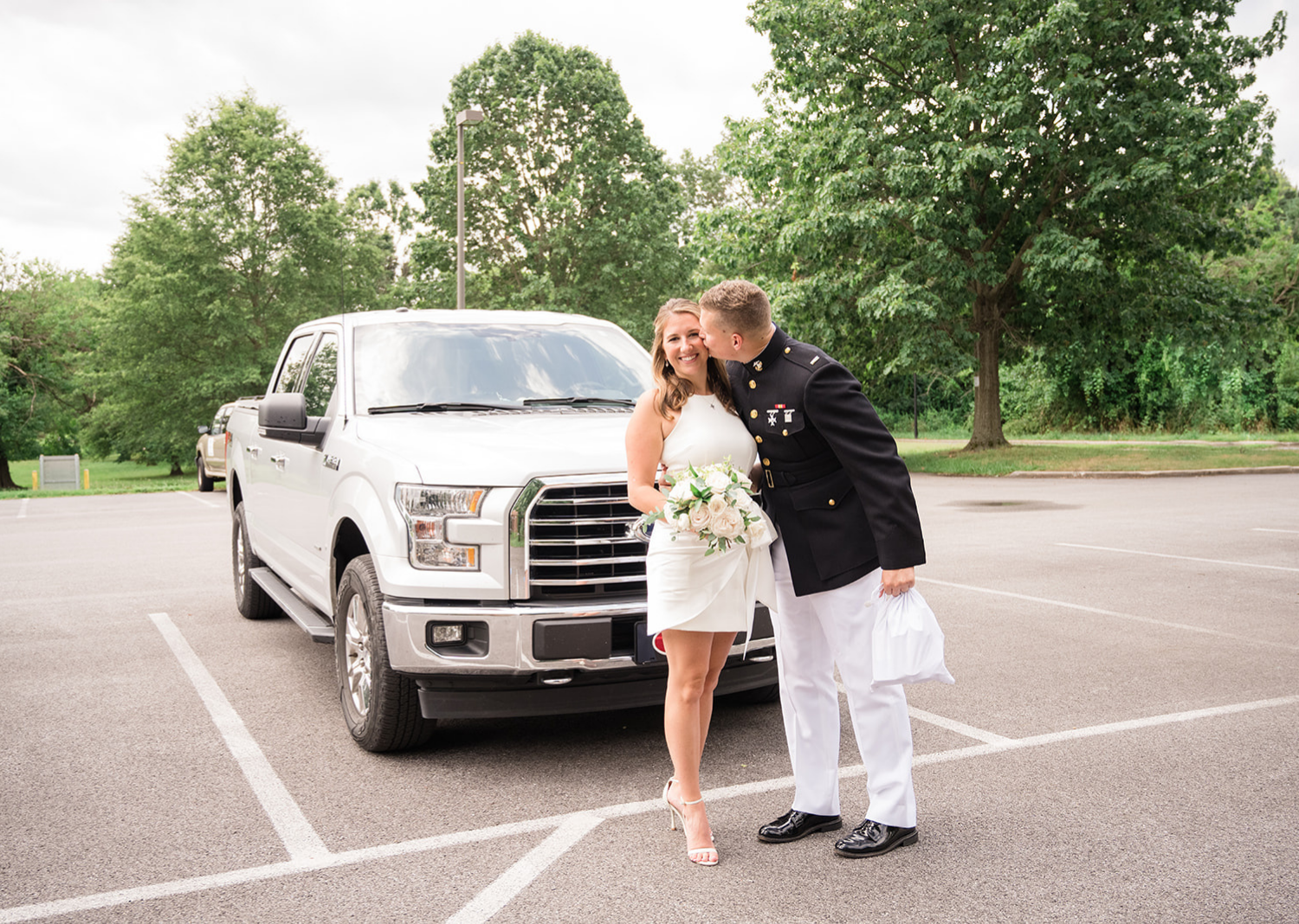 groom kisses his bride on the cheek as they pose i front of their white truck 