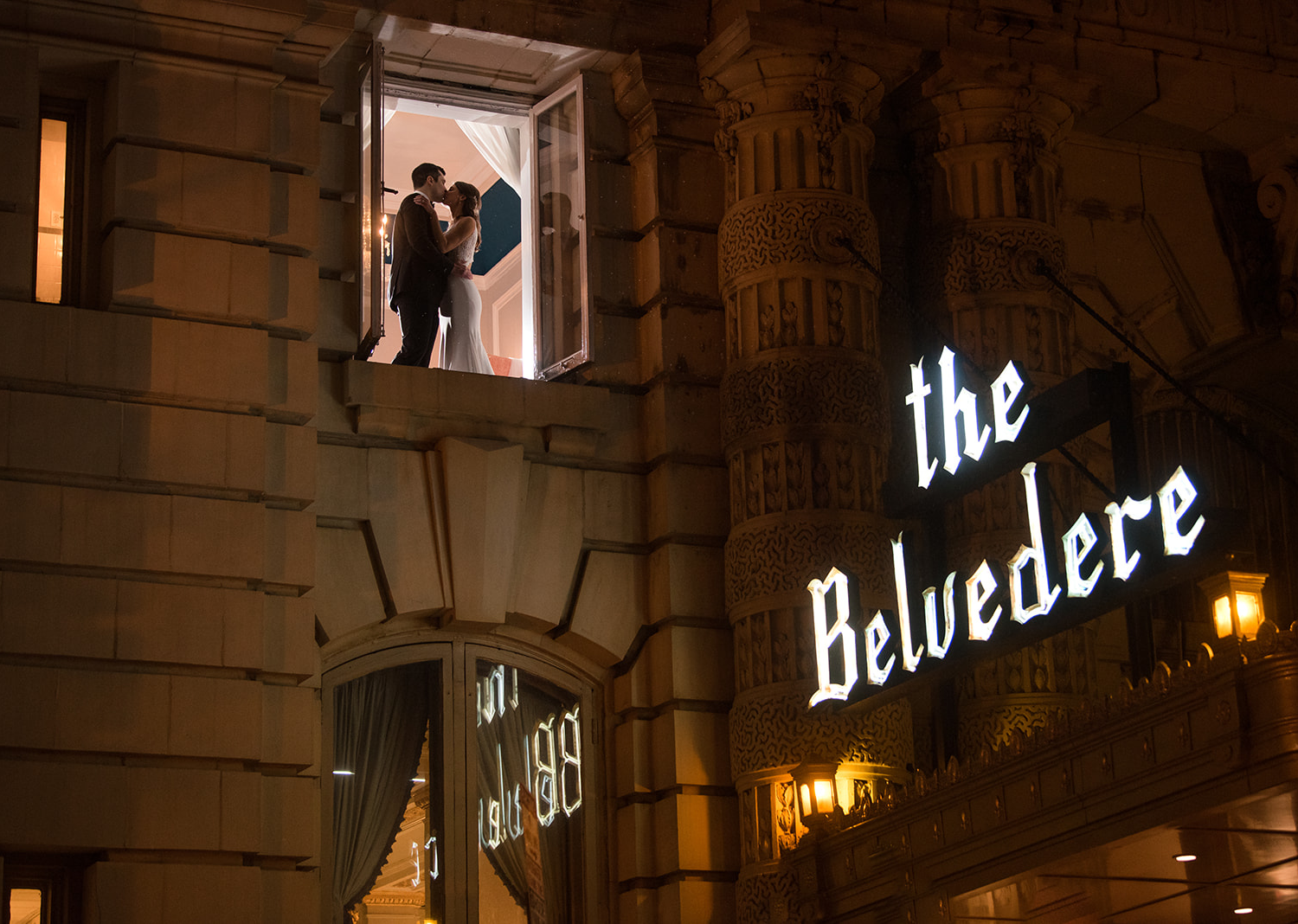 bride and groom share a kiss as they are photographed through a window of the Belvedere hotel