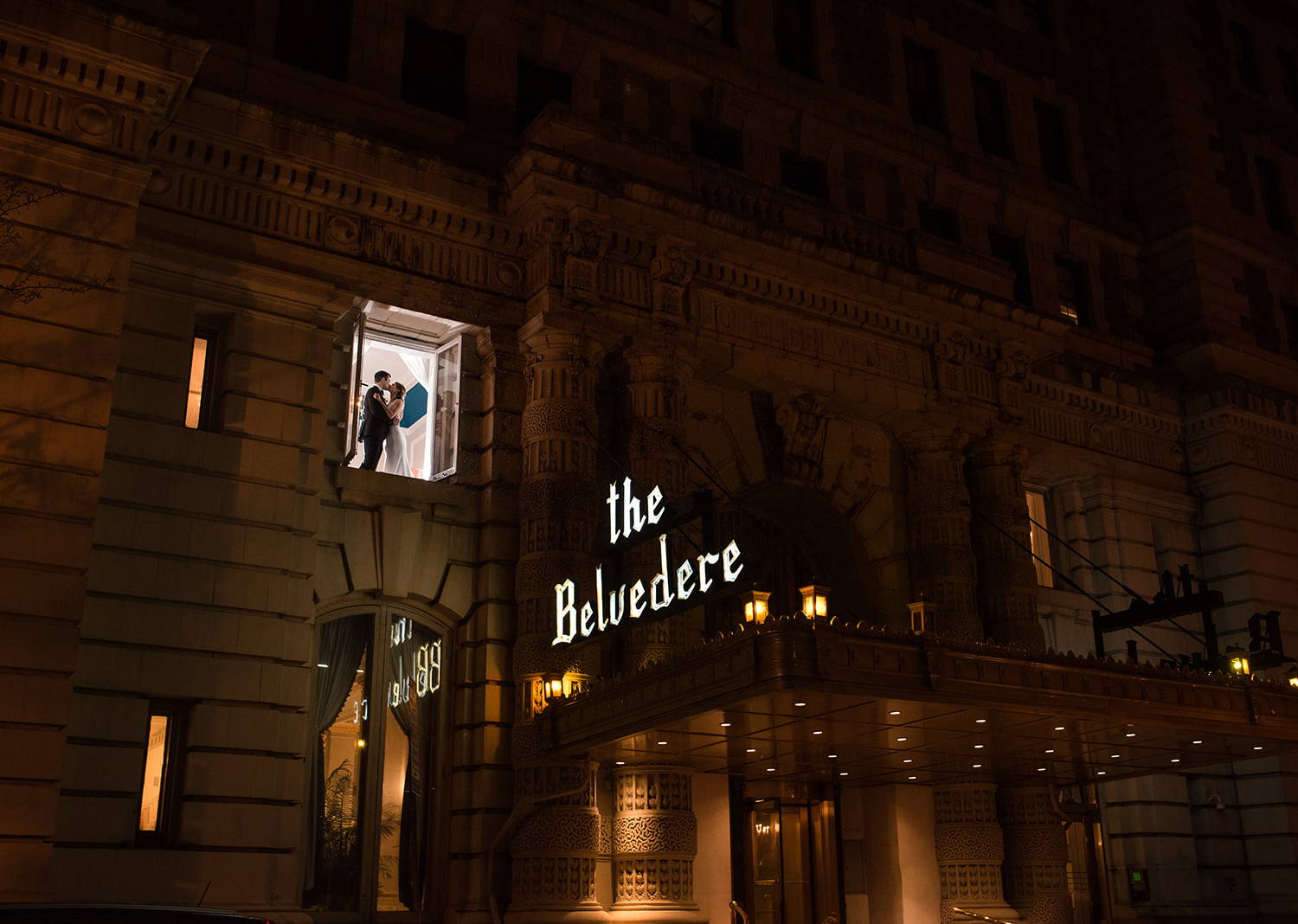 bride and groom share a kiss as they are photographed through a window of the Belvedere hotel