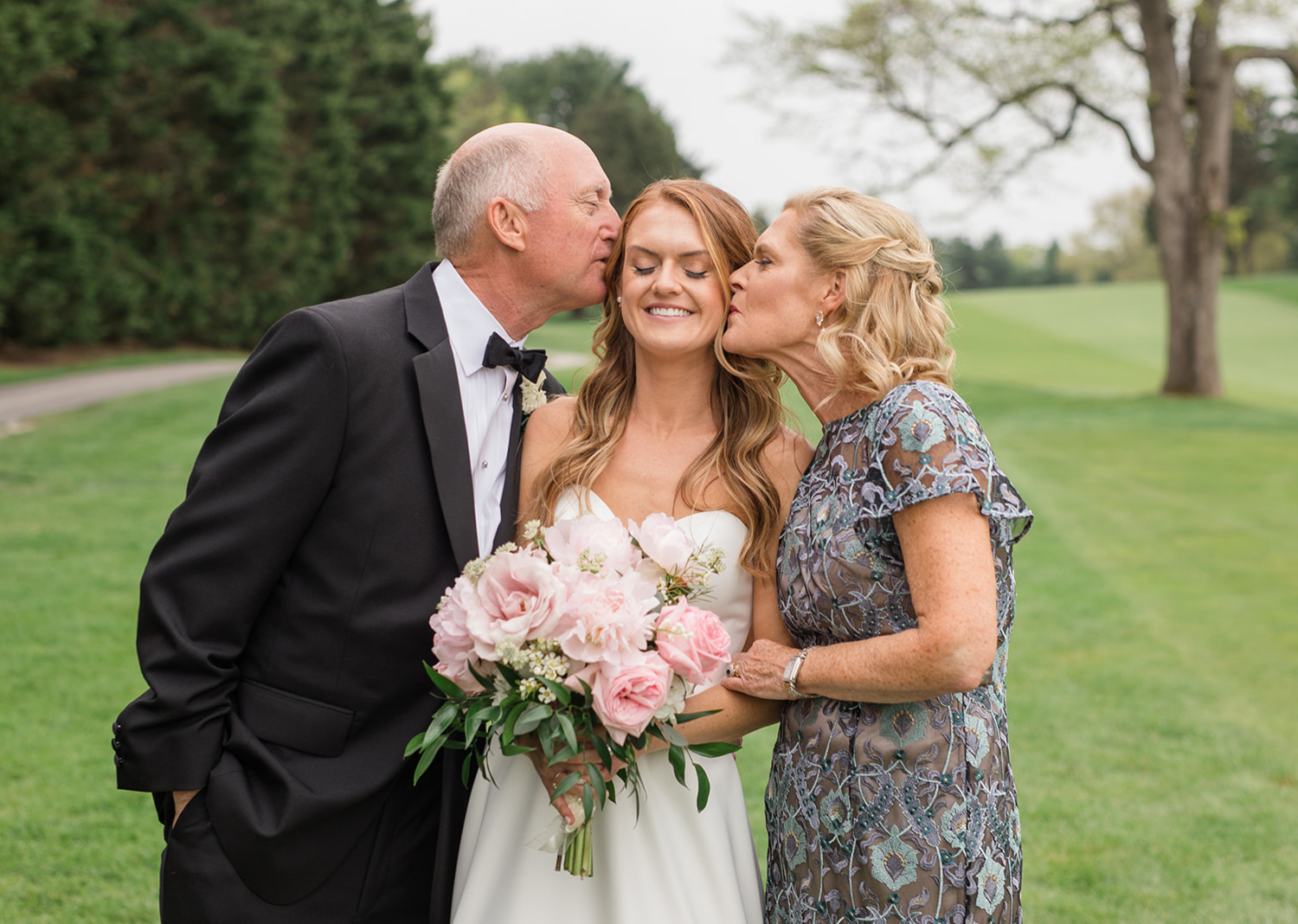 mother and father of the bride give bride a kiss on the cheek