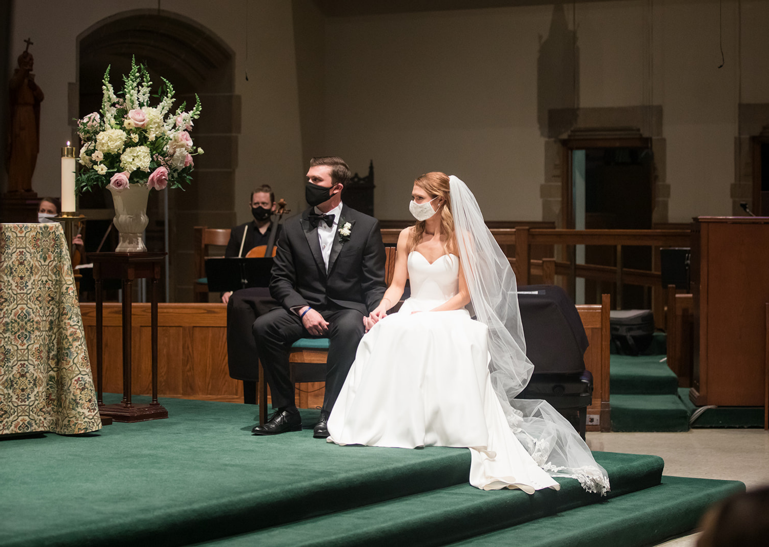 bride and groom sit down at the church for their wedding ceremony as their wearing masks 