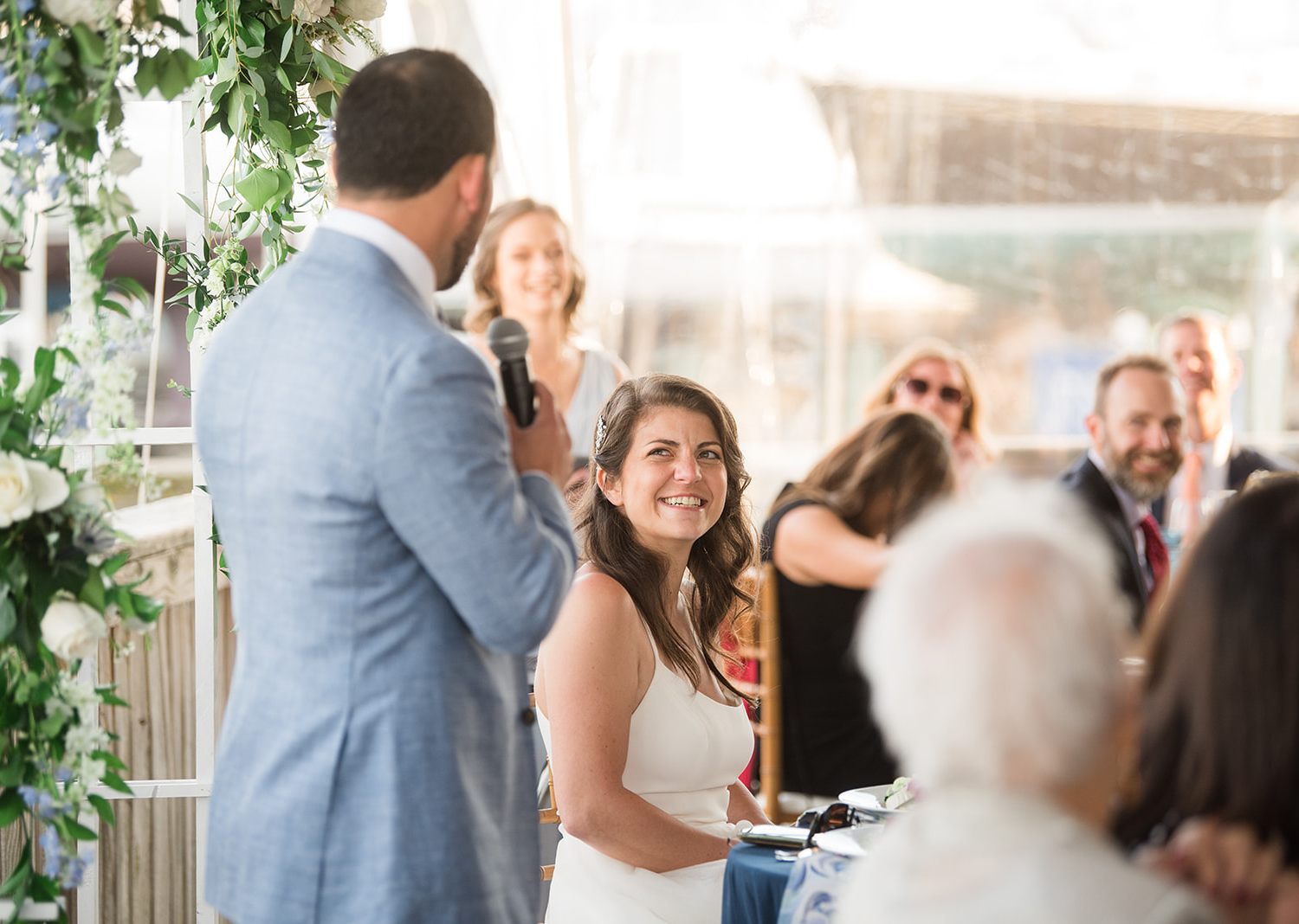 bride smiles as groom gives a speech