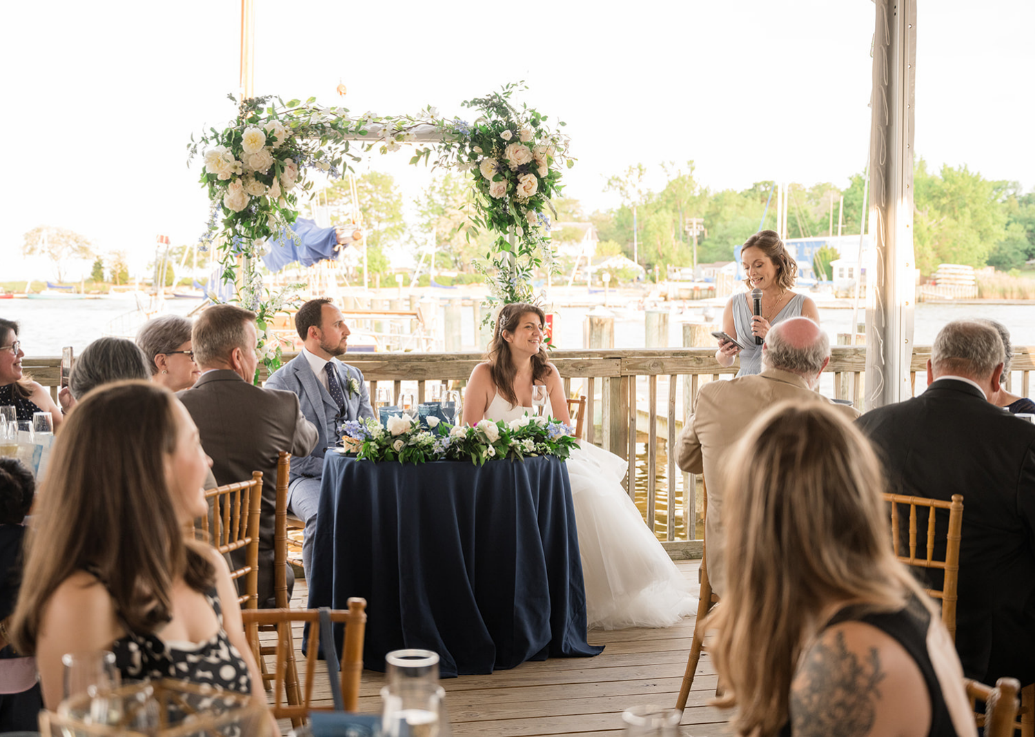 bride and groom smile as bridesmaid gives a wedding speec