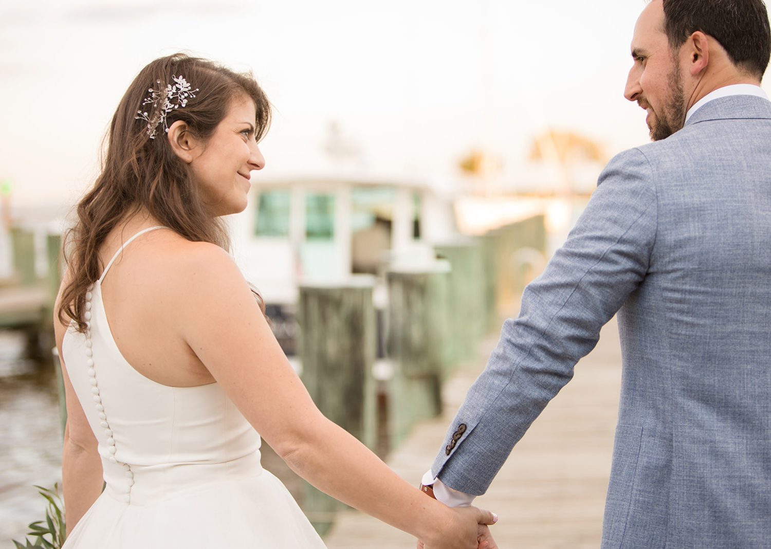 bride and groom smile lookign at eachother as they walk down the pier 