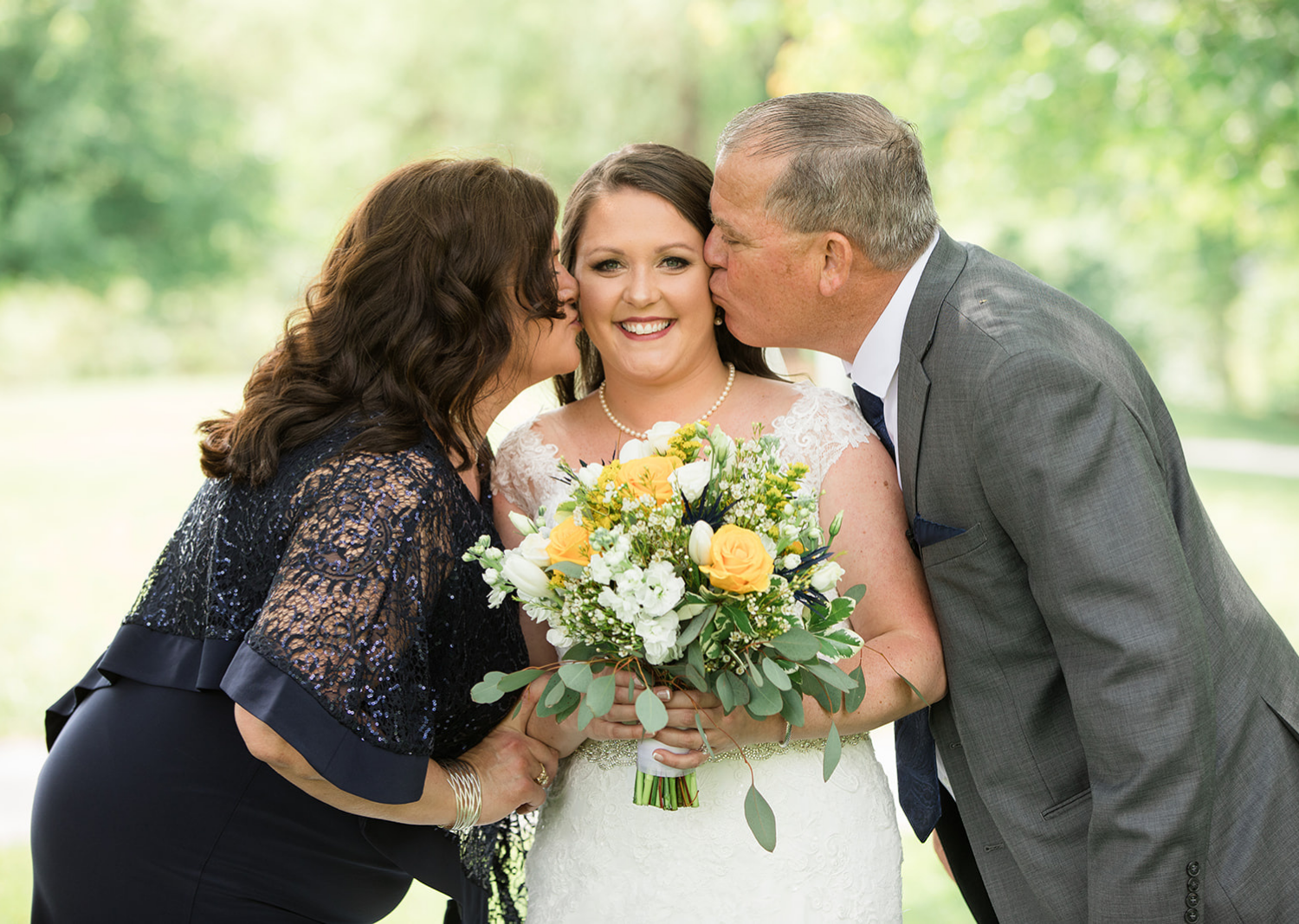 father and mother of the bride kiss her on the cheek