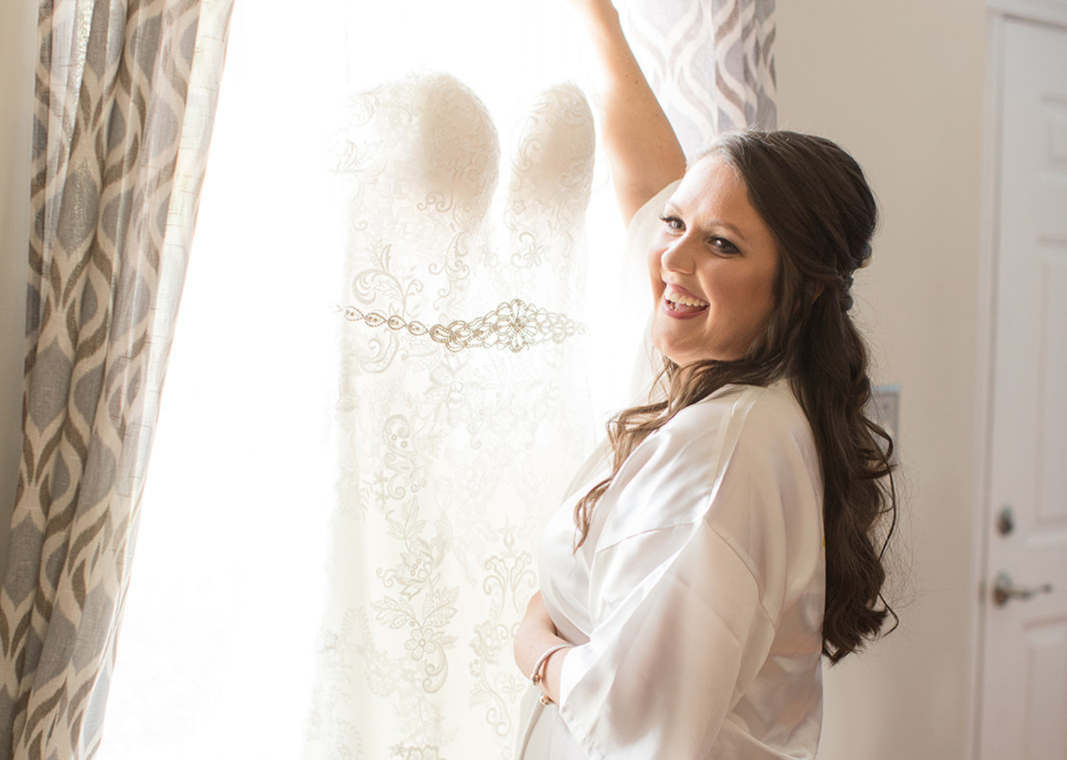 bride looks at her wedding dress as it hangs on the window