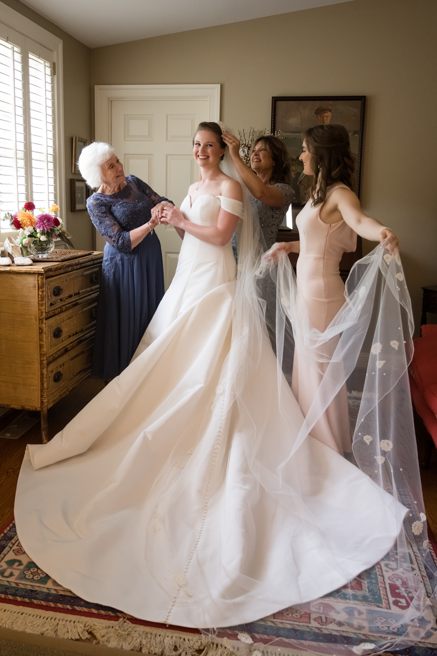 The bride standing with three women as they fix her veil.