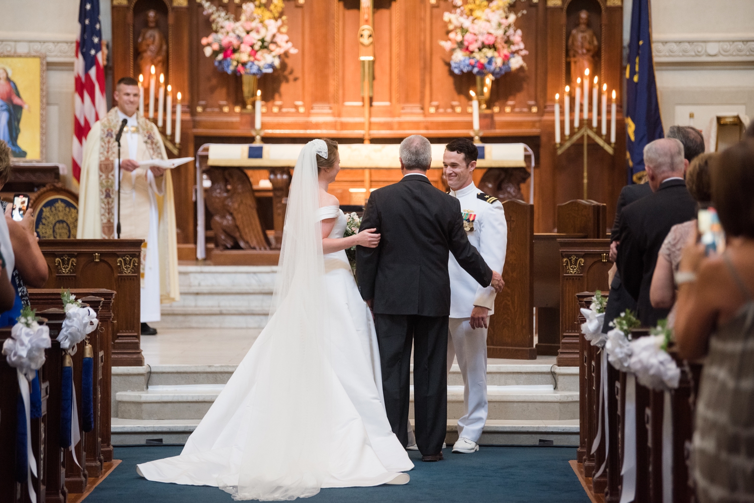 The groom smiles at the bride's father as they greet each other at the end of the aisle.