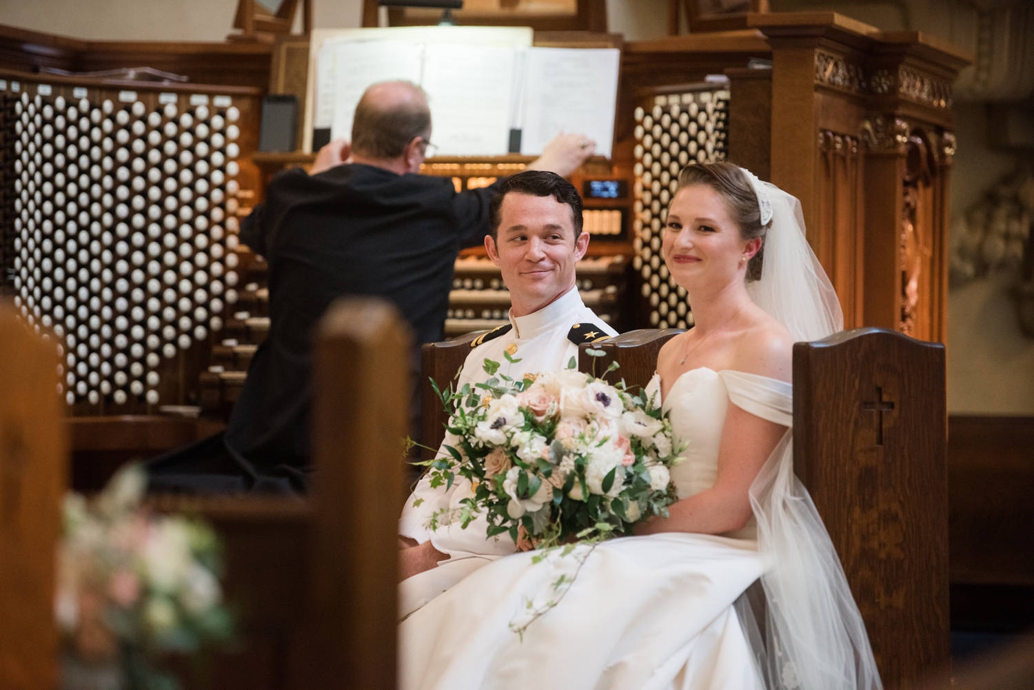 The bride and groom sit together during the ceremony. The groom looks at her lovingly.