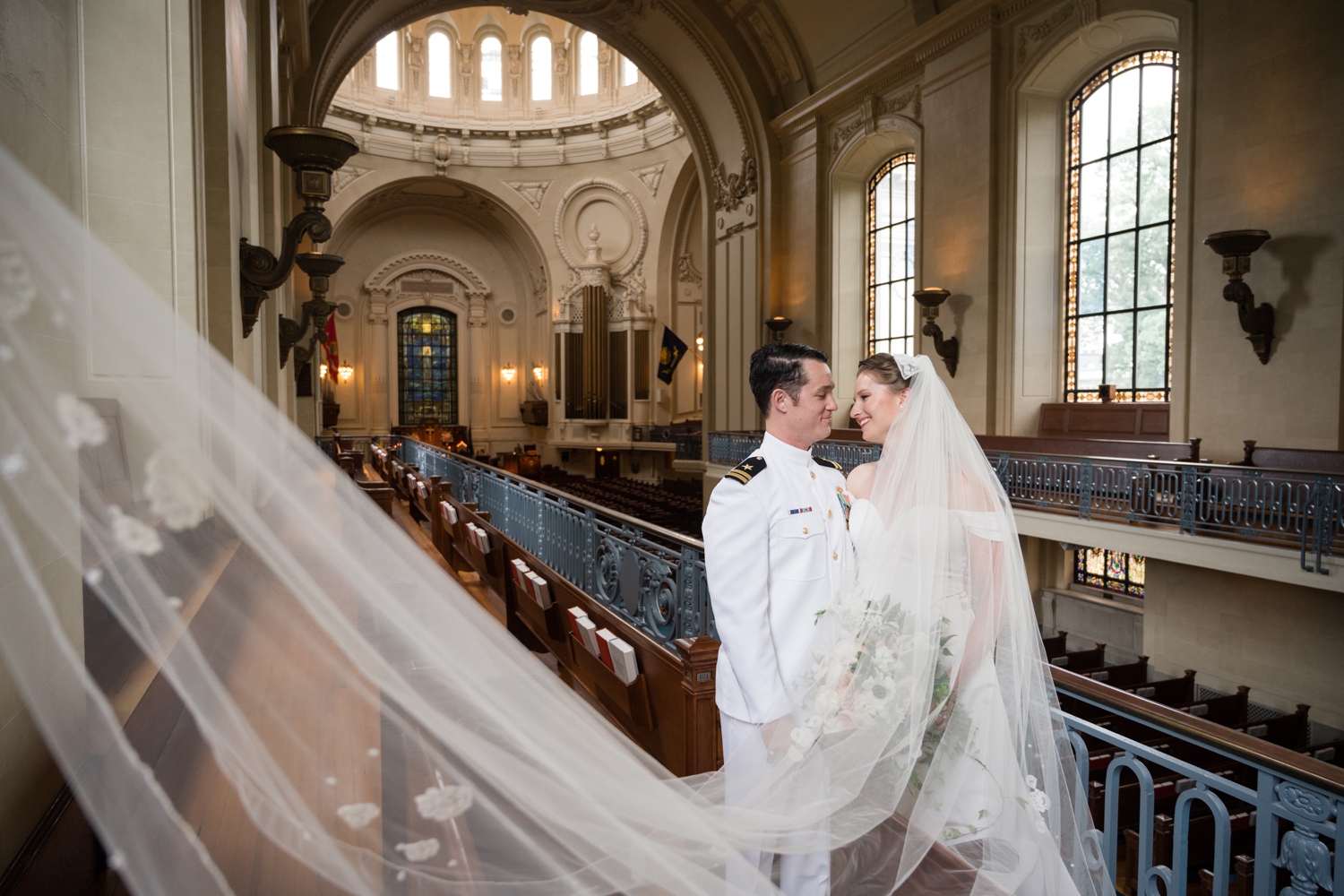 Bride and groom stand close in the church; her veil sweeping into the mid-left side of the frame