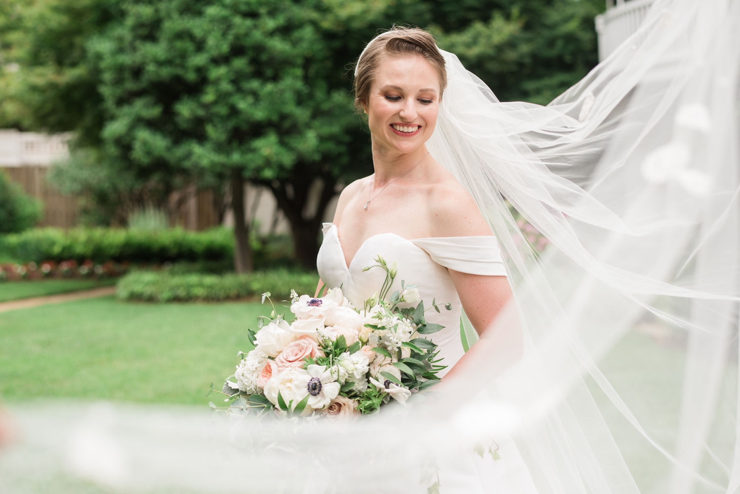 bride smiles, eyes cast down with her wind swept veil