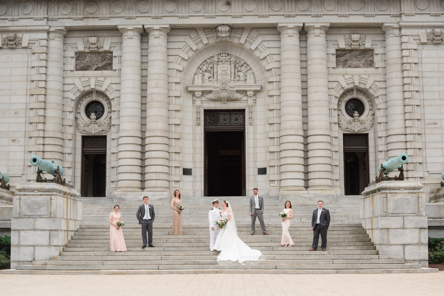 bridal party poses with bride and groom outside the Naval Chapal