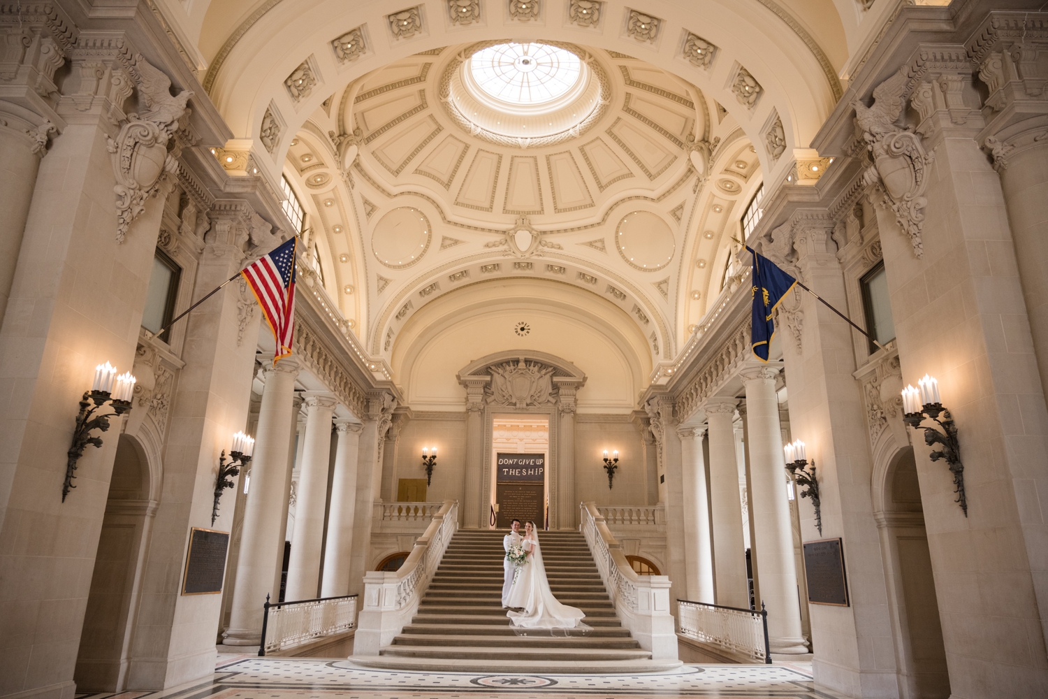 Wide shot of the bride and groom standing on the stairs inside the Naval Chapel where the ornate dome ceiling is featured.