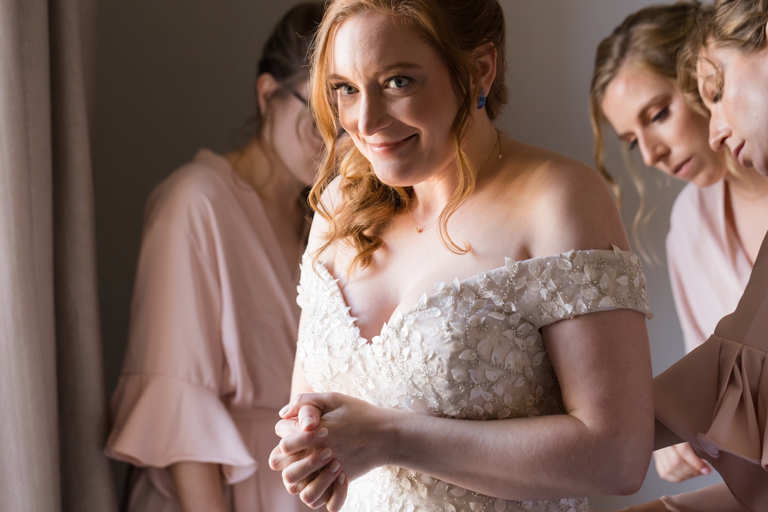 bride smiles as bridesmaids button her dress