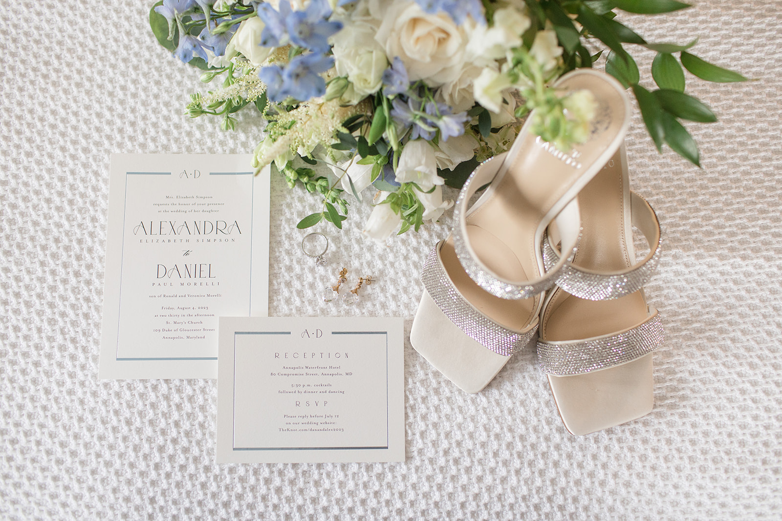 Wedding flat lay with simple white invitations, bridal shoes, and bridal bouquet