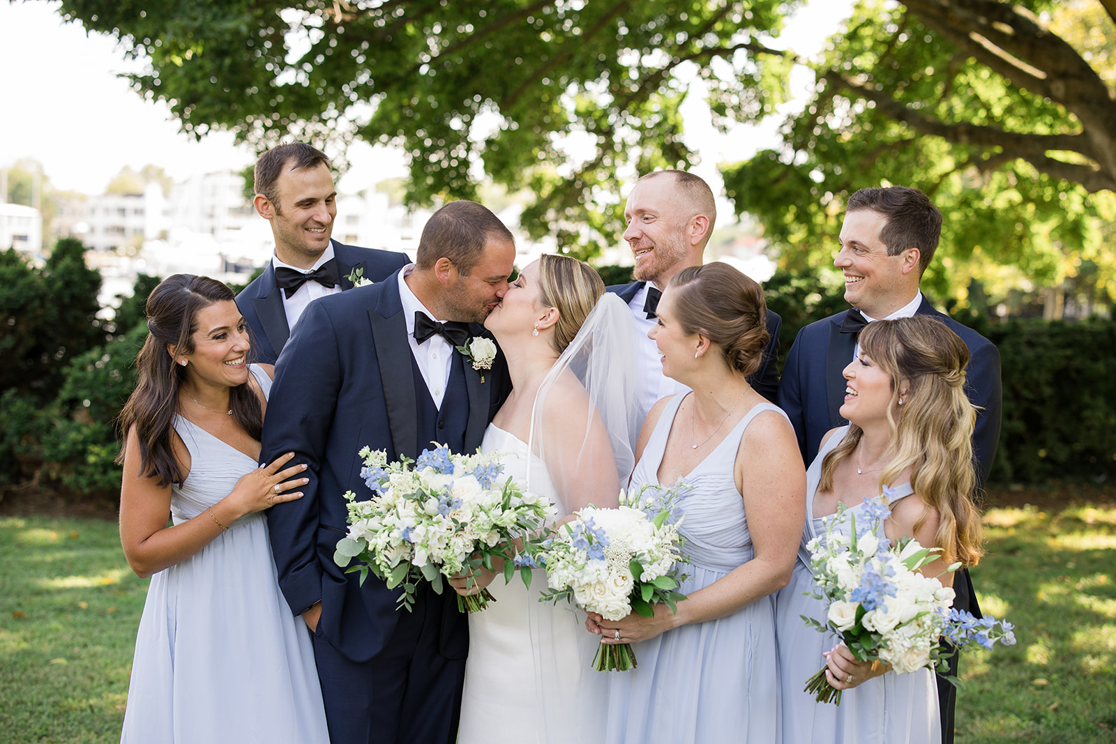 bride and groom kiss while wedding party looks on