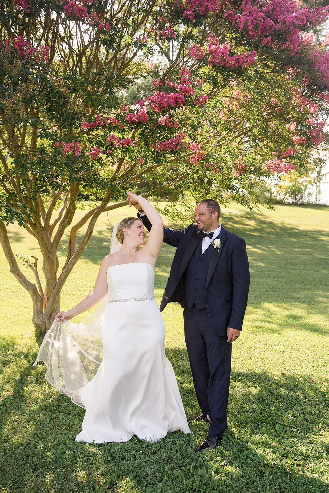 bride does a spin with her groom in grass under blooming tree