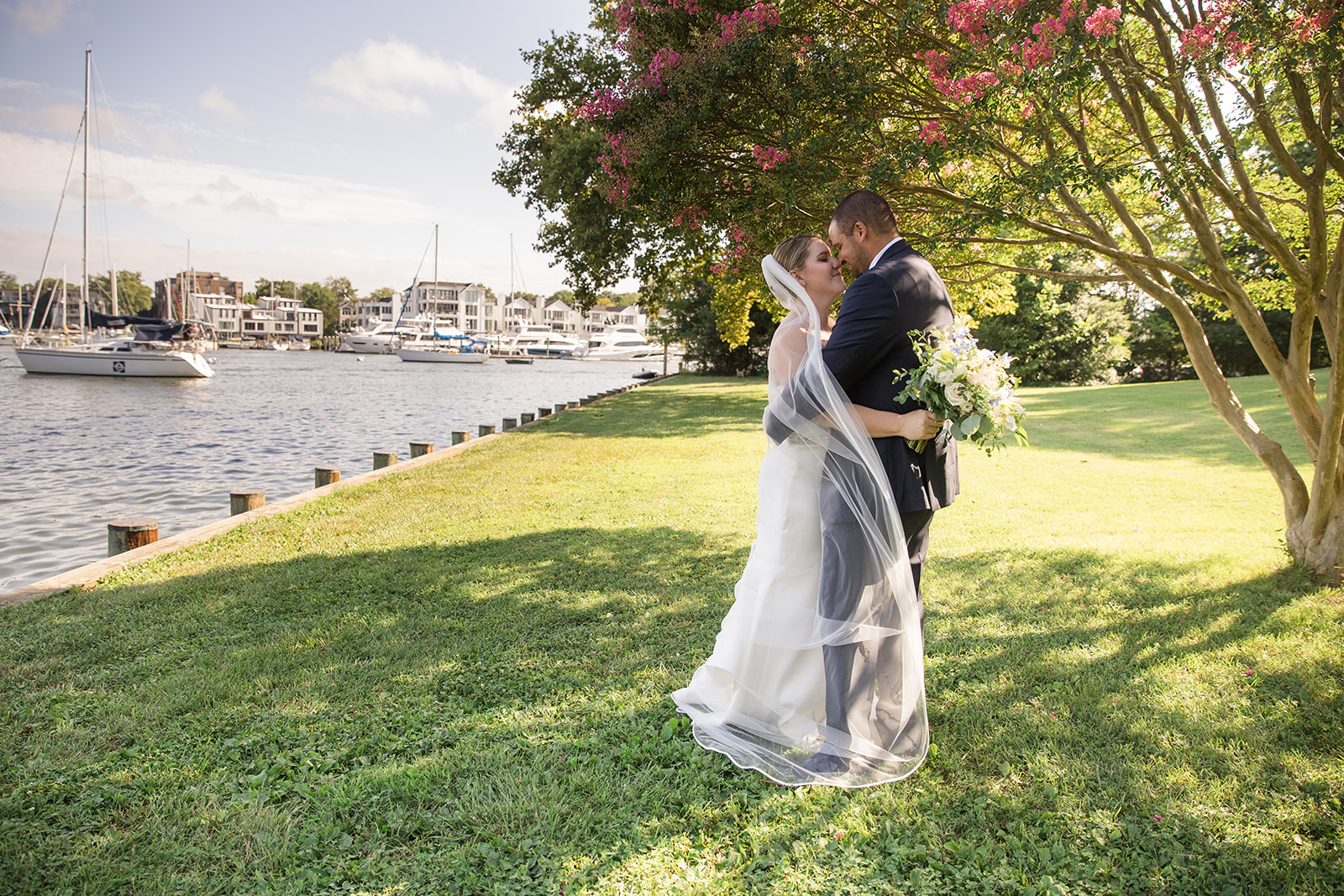 bride and groom portrait in grass under blooming tree on the water