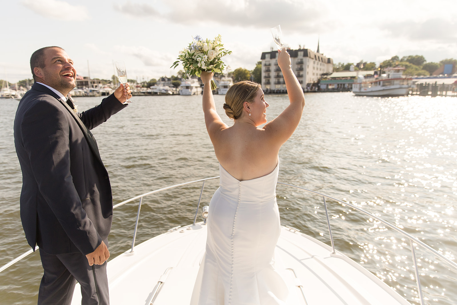 bride and groom cheering on bow of boat