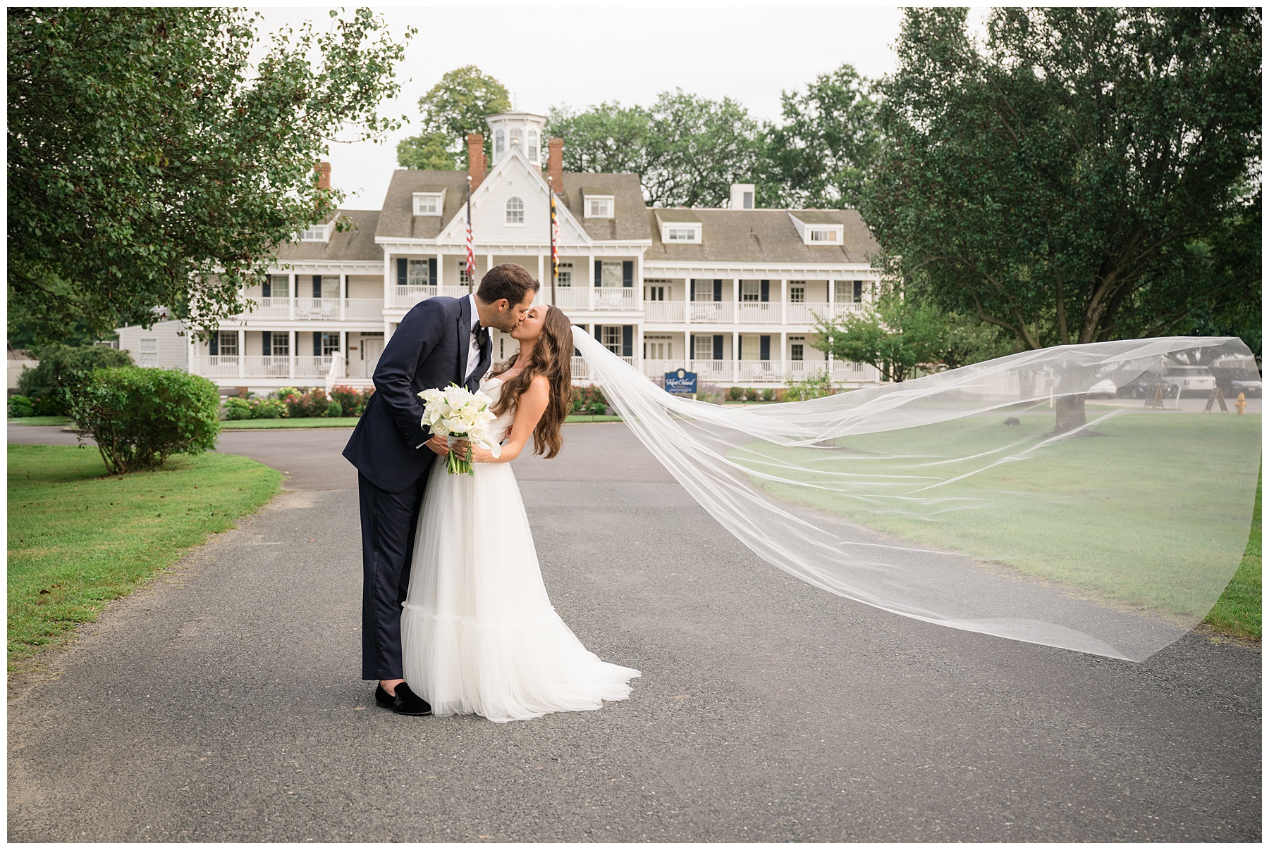 bride and groom kiss in front of kent island resort with veil toss