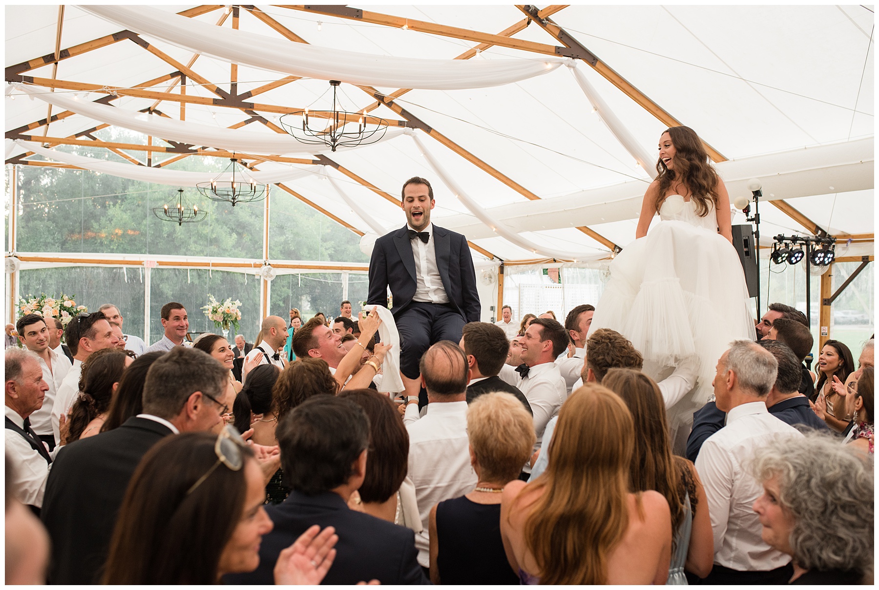 bride and groom lifted in chairs for the horah during jewish wedding reception