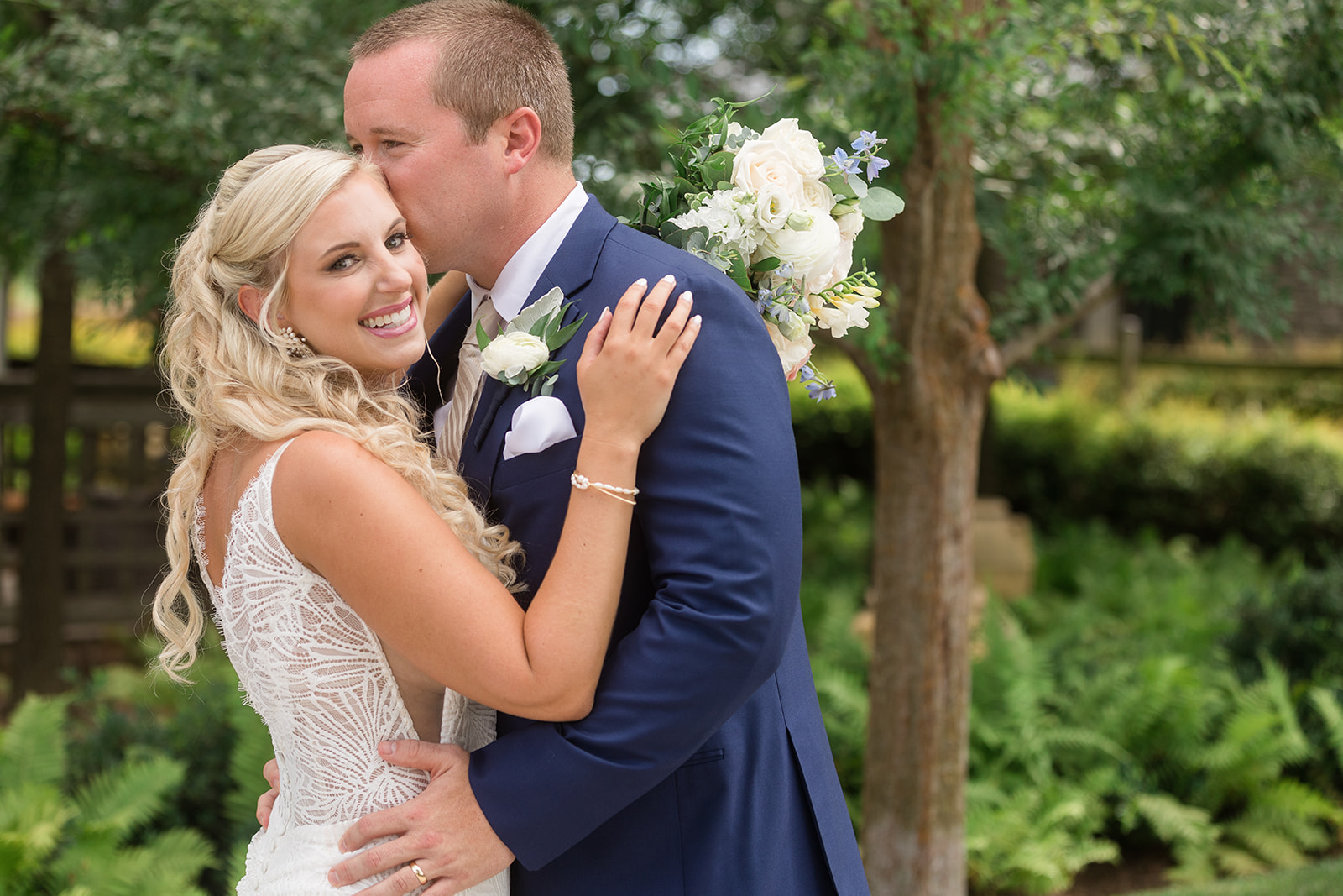 groom kissing bride's temple while bride smiles at camera