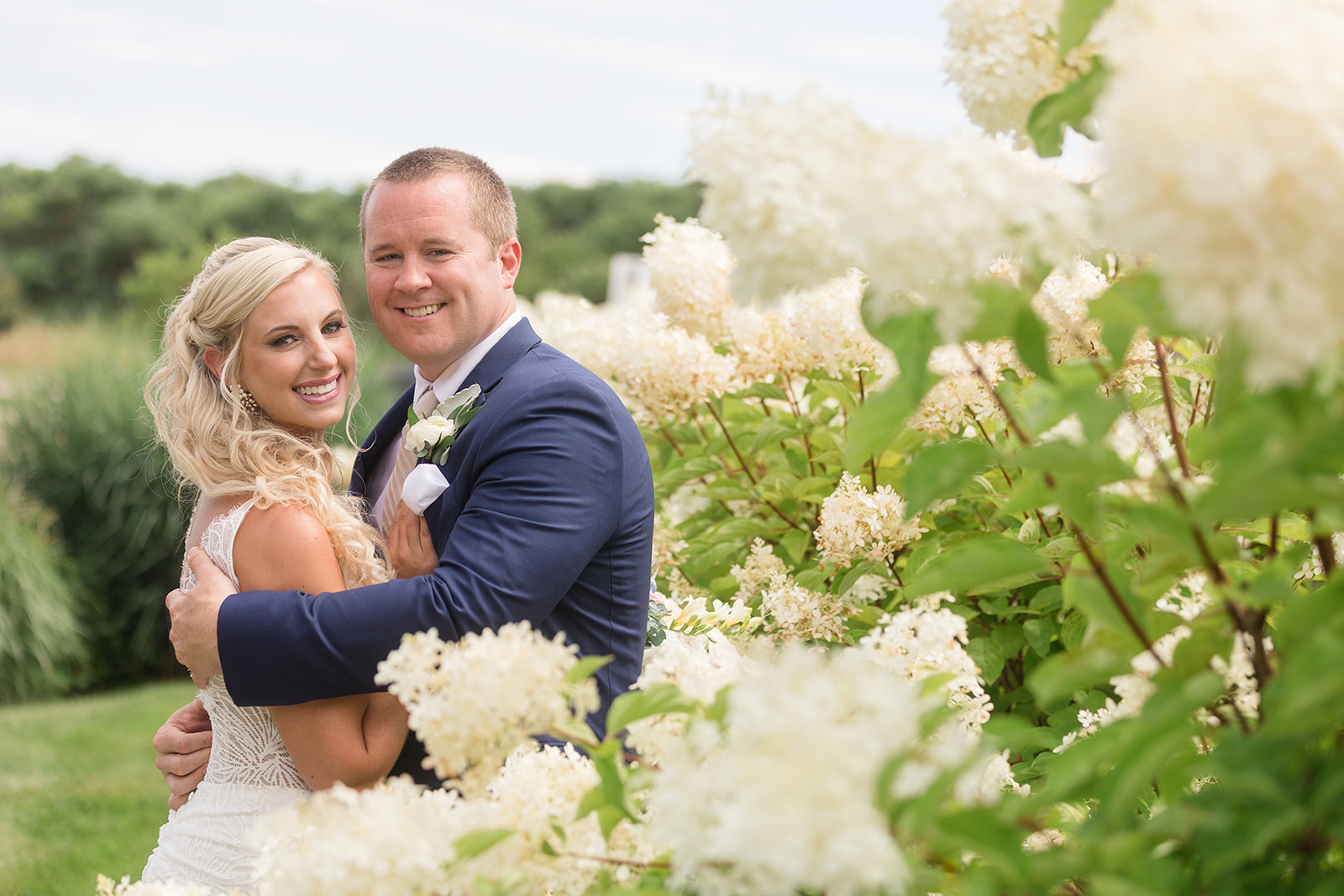 bride and groom embrace among white flowering bushes