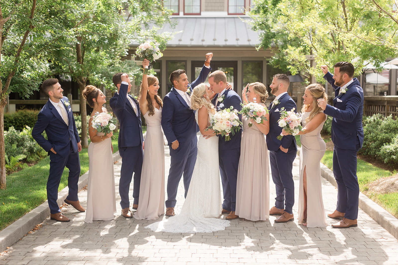 bride and groom kiss while wedding party looks on and cheers