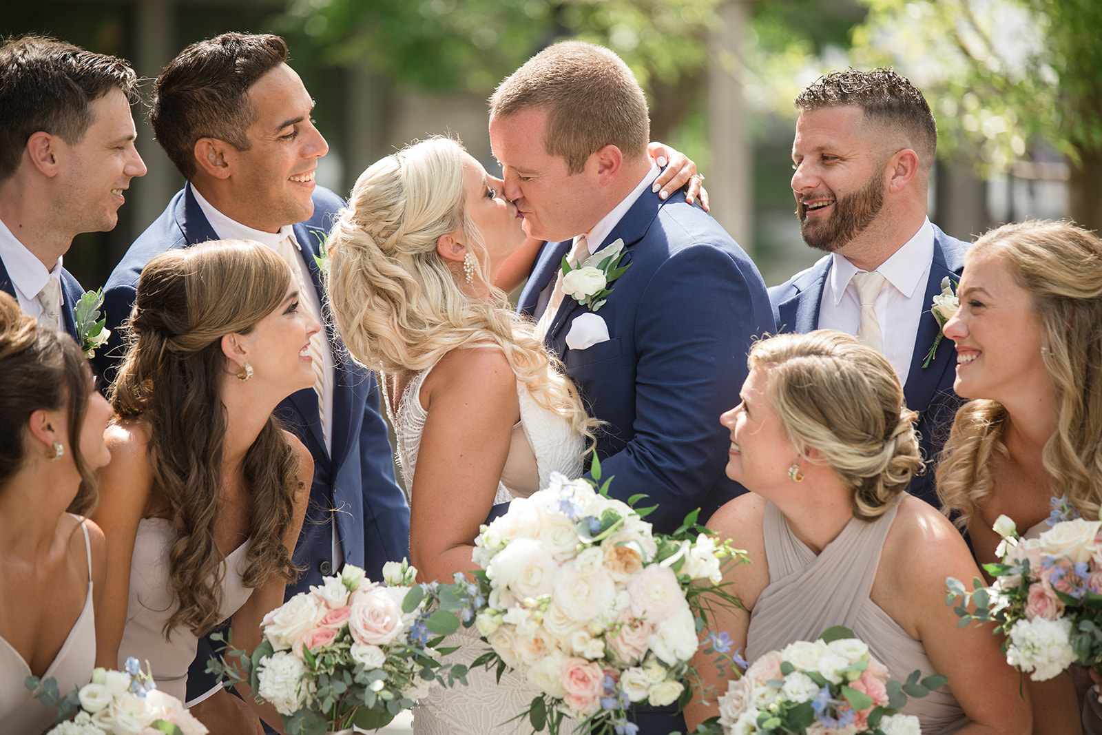 bride and groom kiss while wedding party looks on and smiles