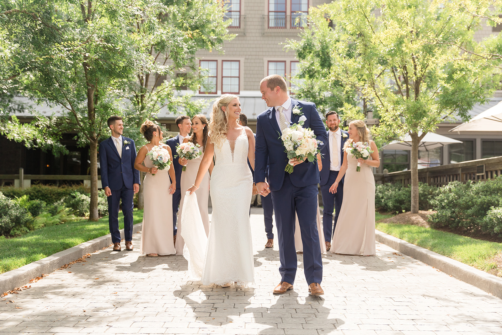 bride and groom walking while looking at each other with wedding party following behind