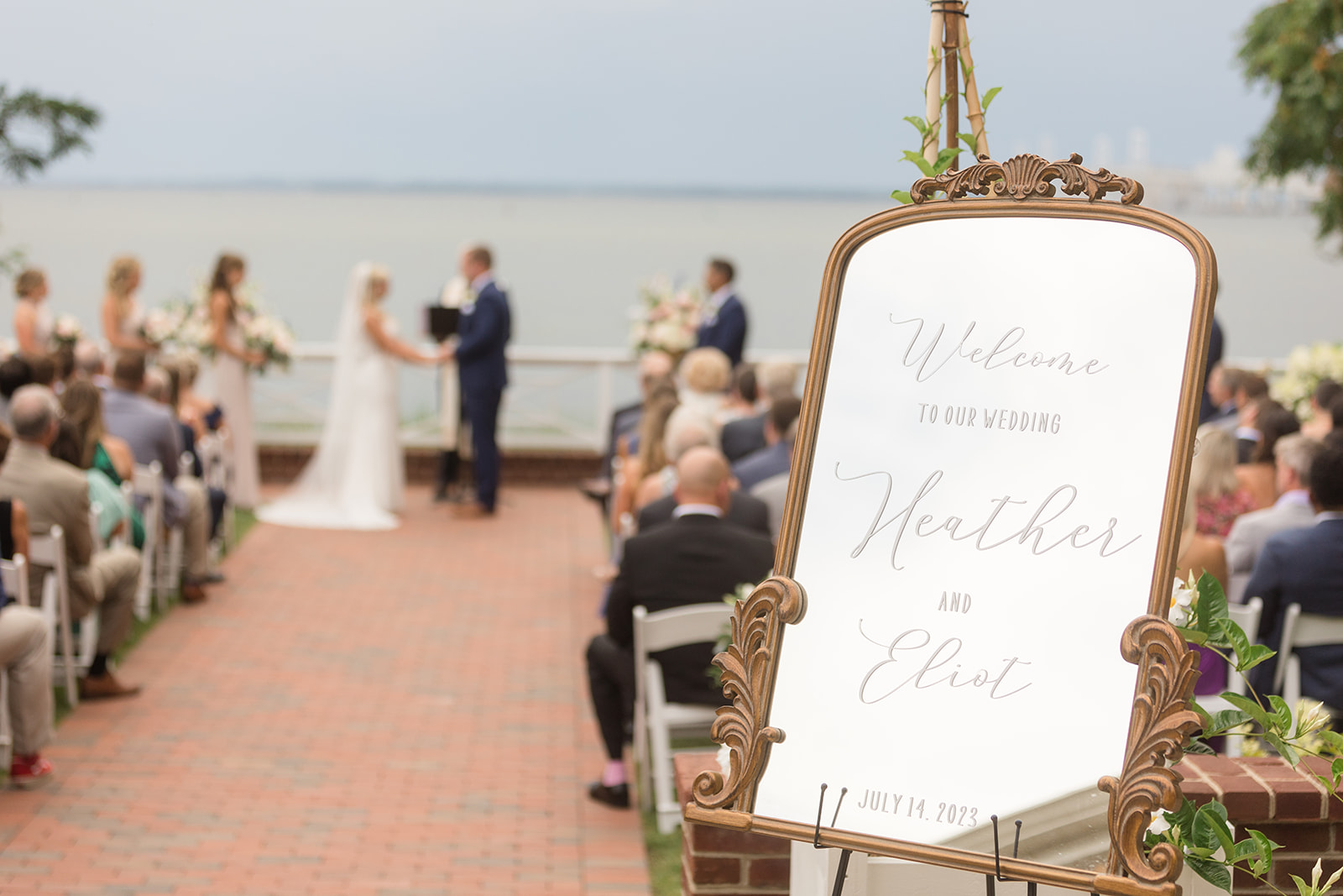 bride and groom during ceremony in background with welcome sign in foreground