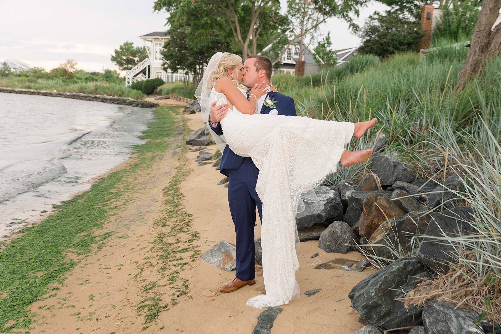 groom holding and kissing bride on sandy beach