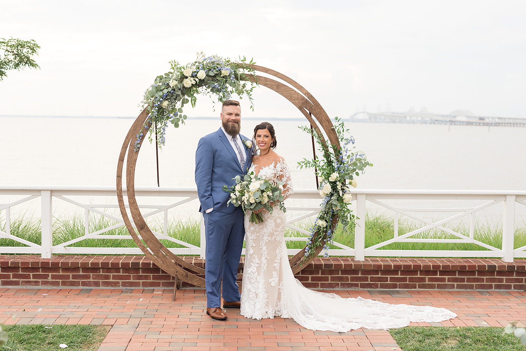 bride and groom under ceremony arbor with chesapeake bay bridge in background