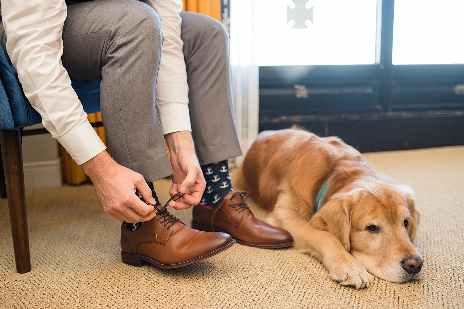 groom tying shoes while dog lays next to his feet