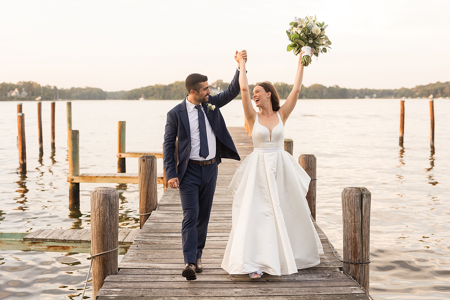 bride and groom on pier at sunset cheer