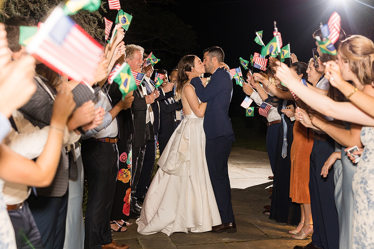 bride and groom exit with guests waving Brazilian flag couple kiss