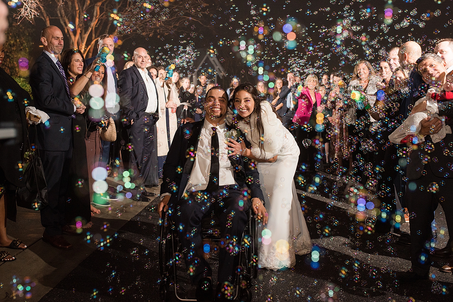 bride and groom smile while surrounded by bubbles and guests exit