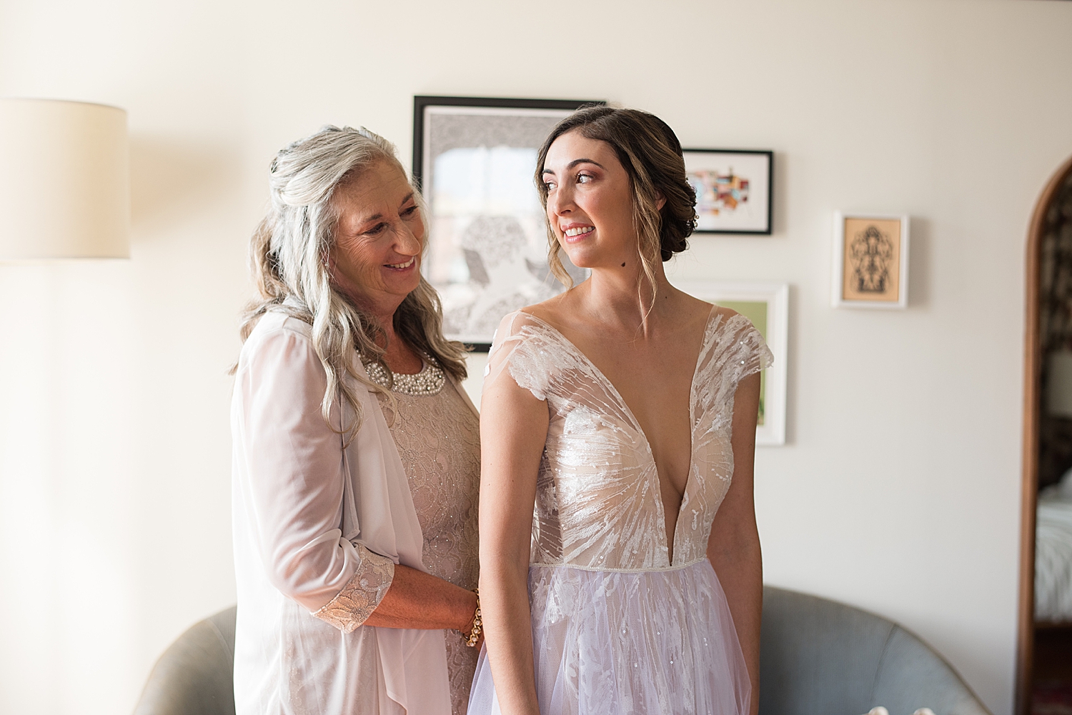 bride's mom helping her get dressed in gown