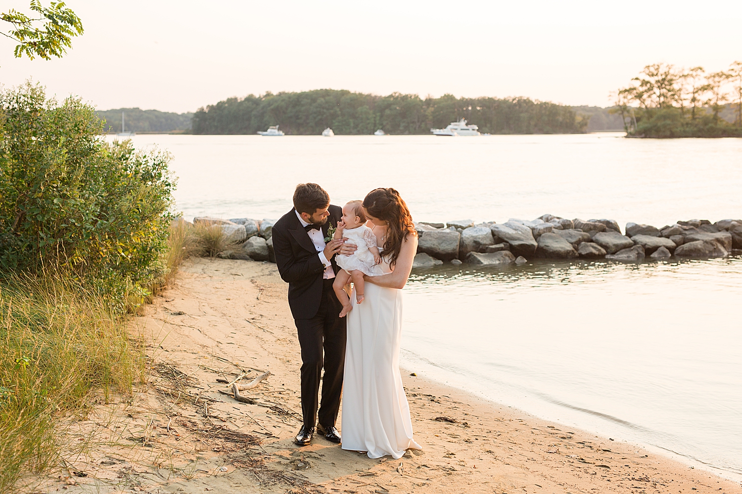 bride and groom with baby on the beach at sunset