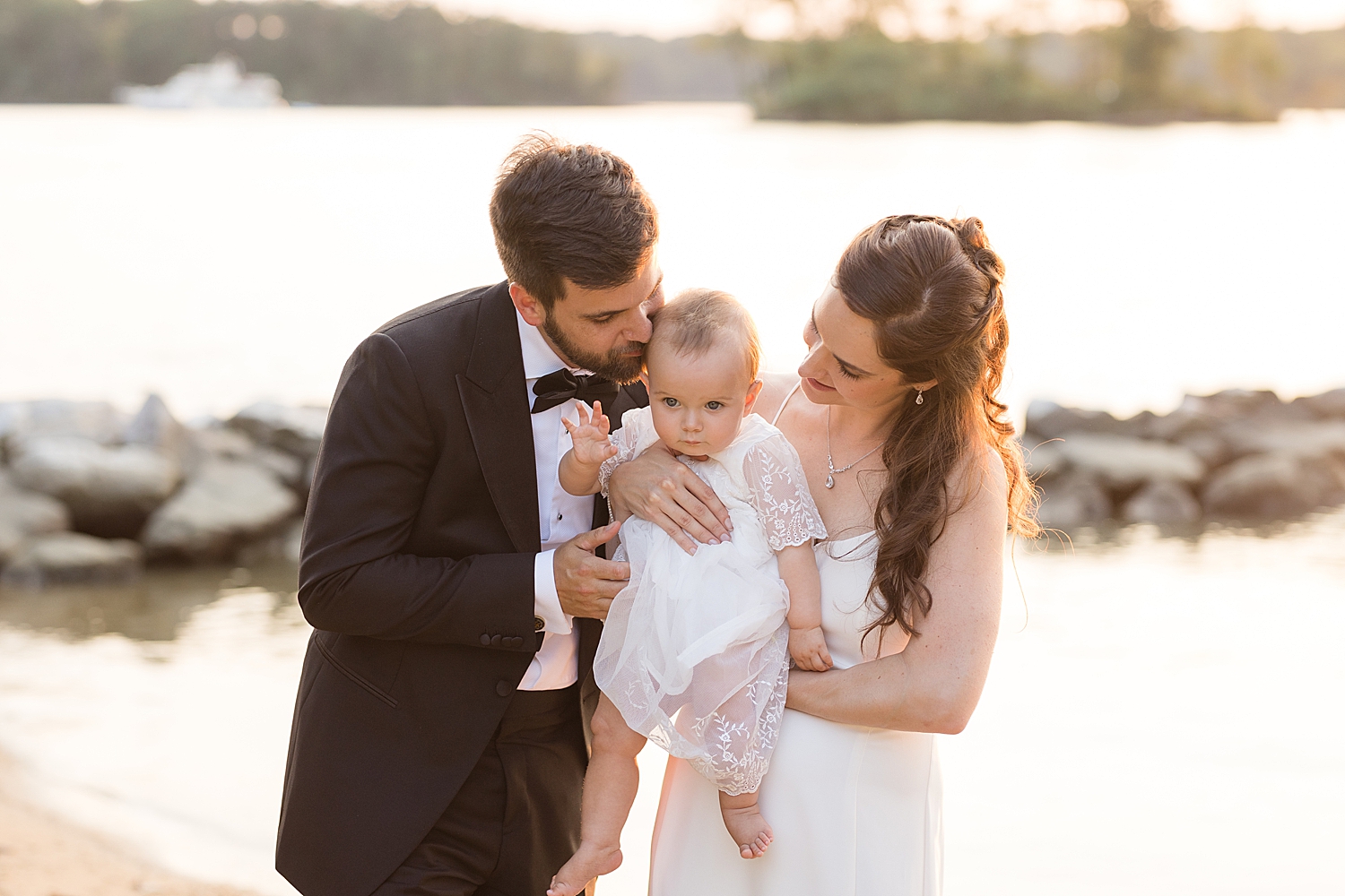 bride and groom with baby on the beach at sunset