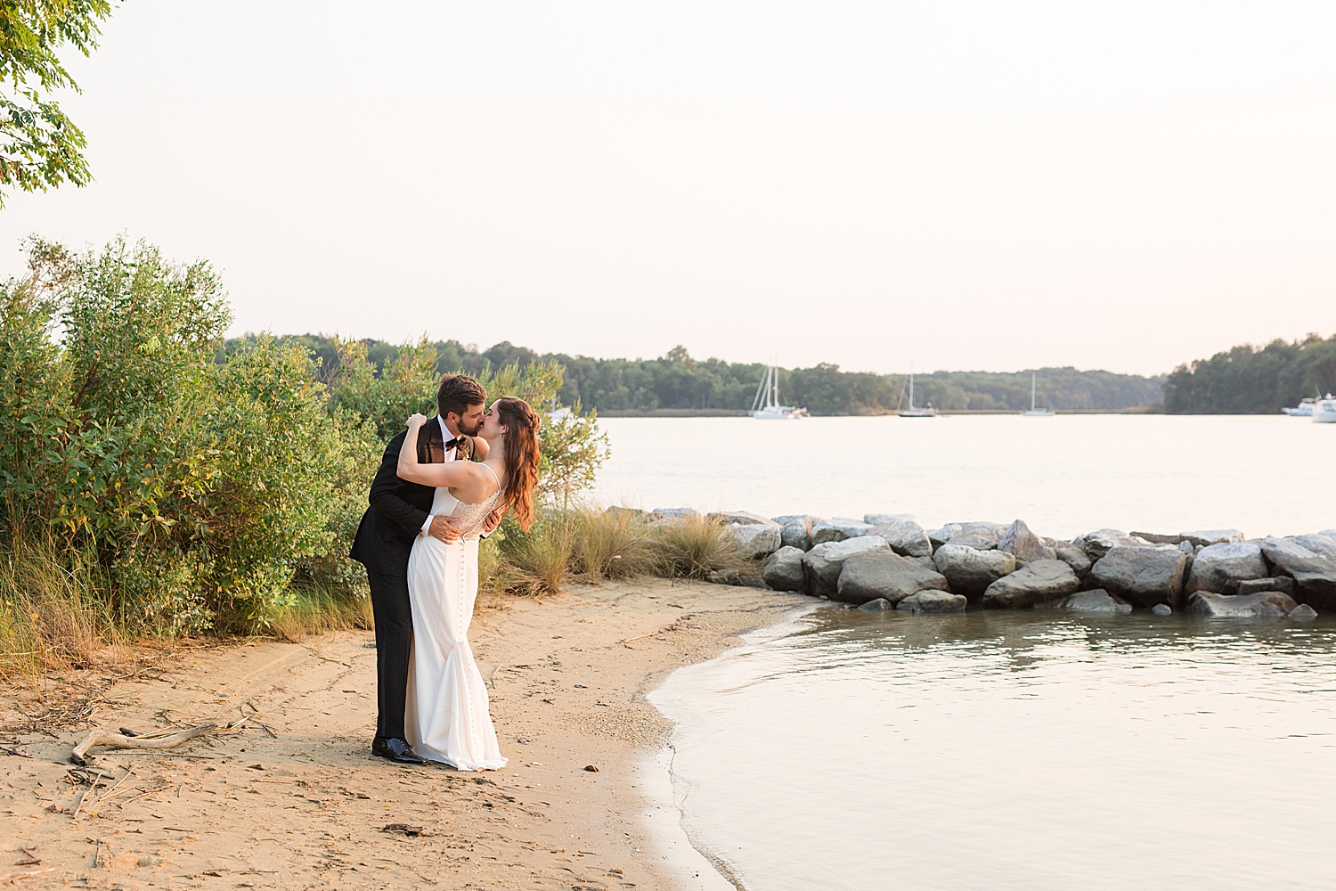 bride and groom kiss on beach at sunset