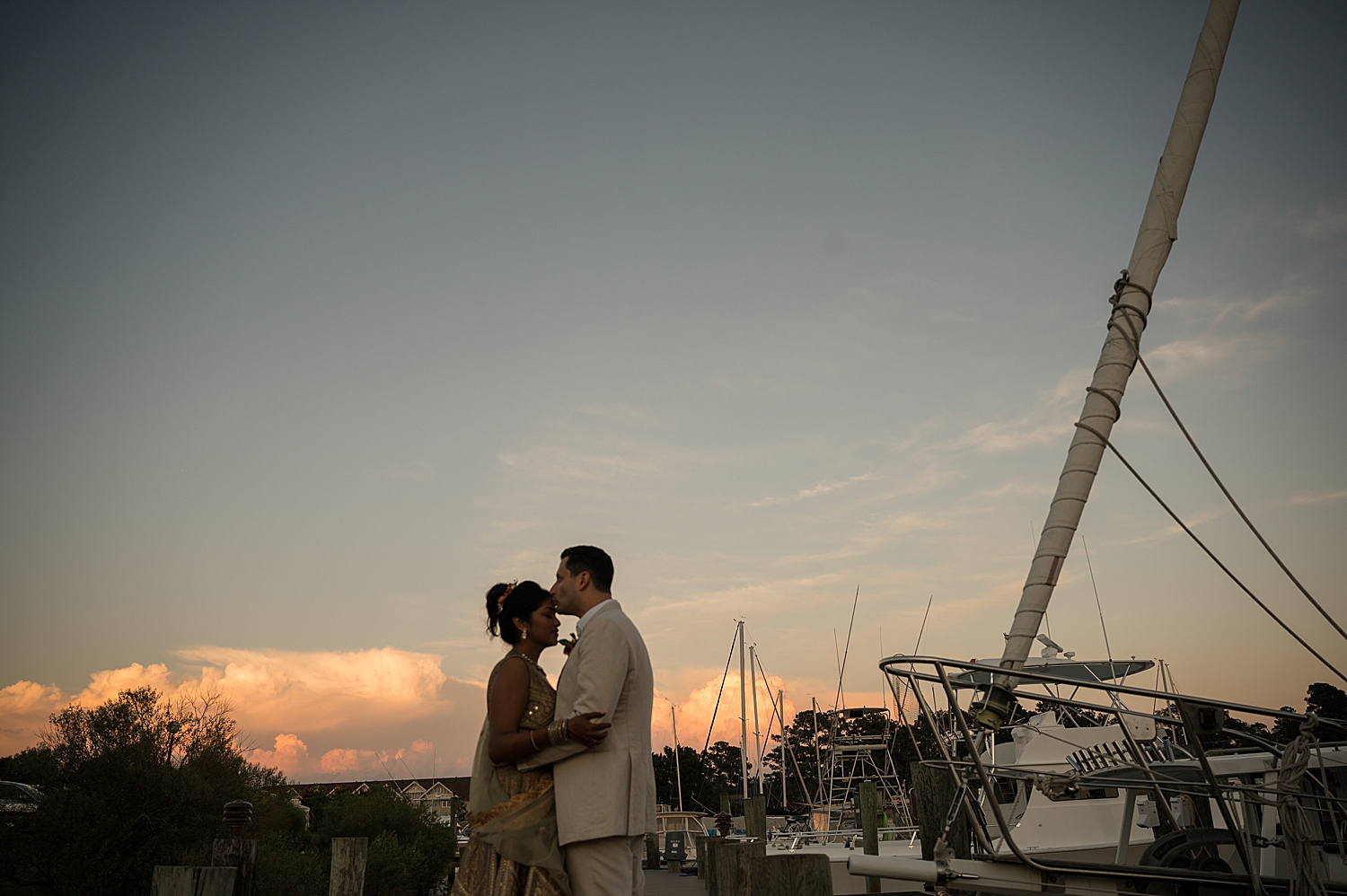 groom kisses bride's forehead at sunset harbor