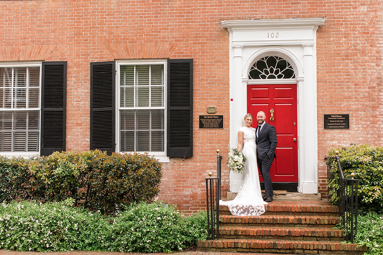 bride and groom in front of brick building with red door